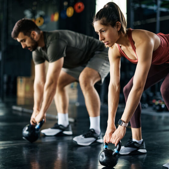 Young athletic couple exercising with kettle bells during cross training at gym.