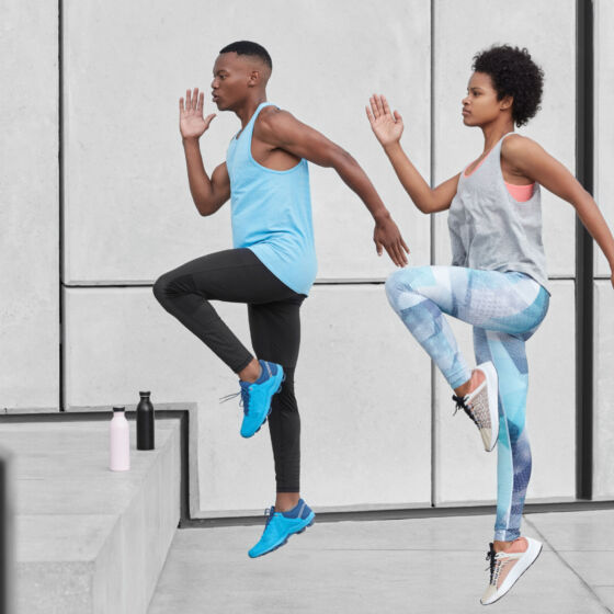 Motivated active ethnic couple run up stairs together, jump highly, train climbing staircase in city, wear comfortable sportsclothes, drink water from bottle, climb challenge, choose difficult path